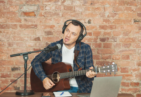Musician recording acoustic performance singing and playing guitar with microphone and headphonesの写真素材