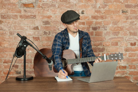 Musician recording acoustic performance singing and playing guitar with microphone and headphonesの写真素材