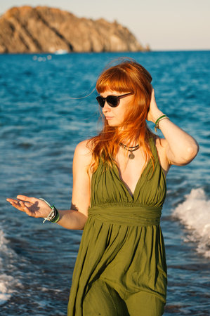 Carefree beautiful redhead woman with sunglasses enjoys summer waves near a scenic tropical beachの写真素材