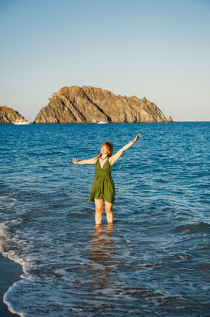Carefree beautiful redhead woman enjoys summer waves near a scenic tropical beachの写真素材