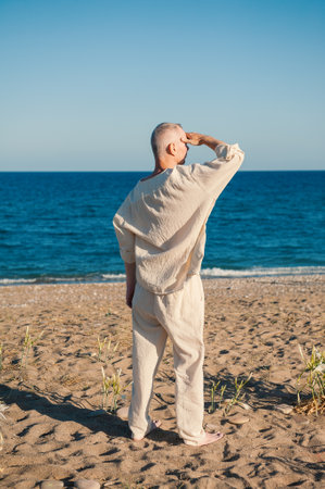 Barefoot mature man in white linen gazes at the serene ocean horizonの写真素材