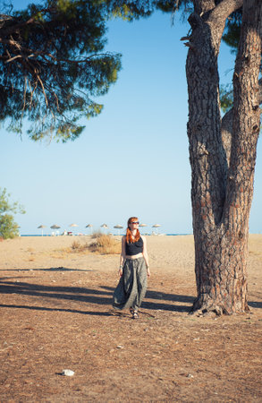 Beautiful redhead woman walking confidently through a sunny landscape, bohemian outfitの写真素材