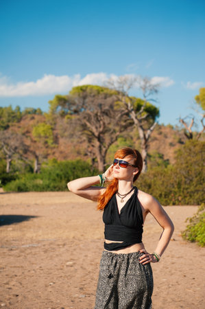 Redhead woman standing confidently in a sunny landscape, bohemian outfitの写真素材