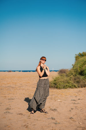 Stylish beautiful redhaired woman in sunglasses enjoys a tranquil moment by the oceanの写真素材