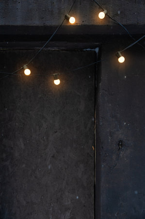 Glowing string lights on a dark concrete wall create a moody and cozy ambiance. Industrial textured...