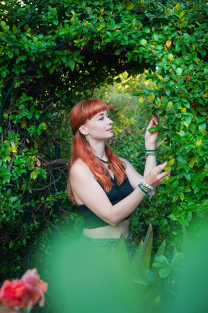 Stylish beautiful redhair woman poses amid vibrant garden foliage, showcasing relaxed eleganceの写真素材