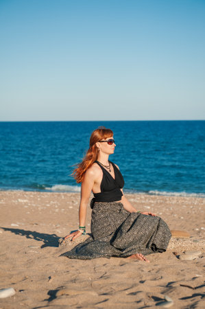 Stylish beautiful redhaired woman in sunglasses enjoys a tranquil moment by the oceanの写真素材