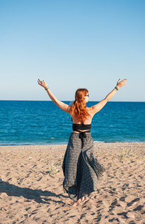 Beautiful woman enjoying freedom on the beach with arms raised, symbolizing carefree summer joyの写真素材