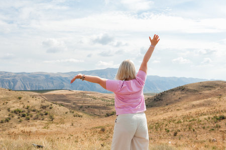 Beautiful woman enjoying the scenic mountains, arms raised in freedom and joyの写真素材