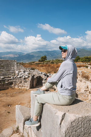 Casual traveler woman enjoying sunny travel moment near ancient ruins and mountainsの写真素材