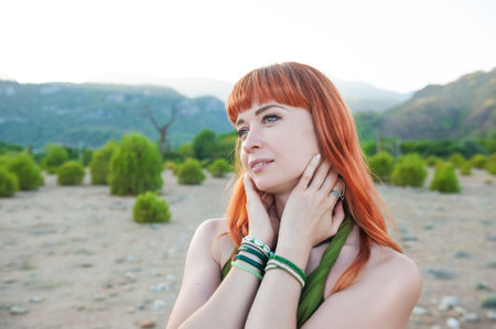 Stylish beautiful redhair woman poses amid desert landscape, showcasing relaxed eleganceの写真素材