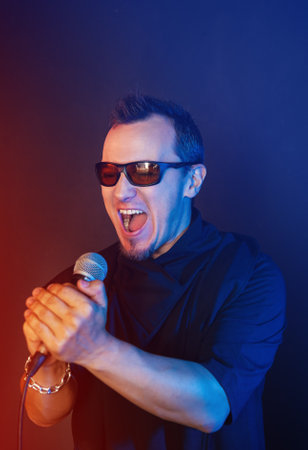 Rock singer man sings with microphone and sunglasses against red and blue backgroundの写真素材