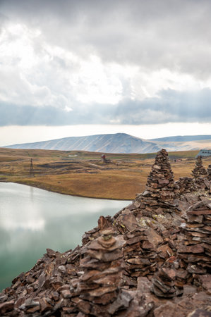 Stacked stone cairns and lake under cloudy sky symbolize tranquility and balanceの写真素材