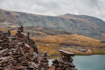 Stacked stone cairns and lake under cloudy sky symbolize tranquility and balanceの写真素材