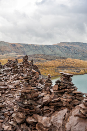 Stacked stone cairns and lake under cloudy sky symbolize tranquility and balanceの写真素材