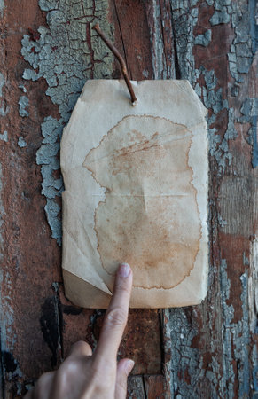 Old vintage paper advertisement hanging on aged wall nailed by rusty doornail with human finger pointing on itの写真素材