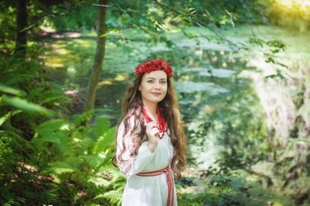 Young smiling woman in a vintage dress with a floral wreath and beads showcases Slavonic style outdoorの写真素材