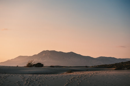 Dramatic twilight colors over peaceful desert landscape at sunset, featuring footprints in the soft sandの写真素材