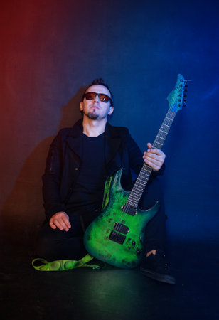 Musician rock guitarist plays green electric guitar sits against red and blue backgroundの写真素材