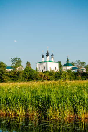 Orthodox church reflects in a calm river surrounded by summer greeneryの写真素材