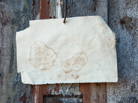 Old vintage paper advertisement hanging on aged wooden wall nailed by rusty doornailの写真素材