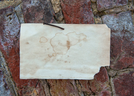 Old vintage paper advertisement hanging on aged red brick wall nailed by rusty doornailの写真素材