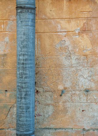 Weathered yellow wall with a rusty metal drainpipe and worn textures