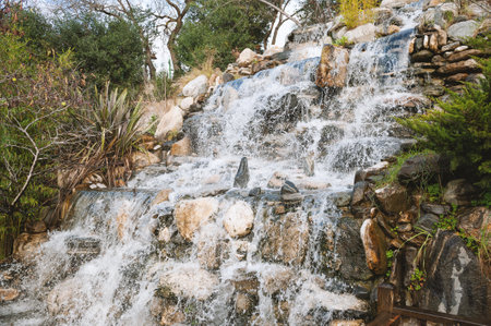 Stone waterfall cascades through lush tropical plants in a peaceful gardenの写真素材