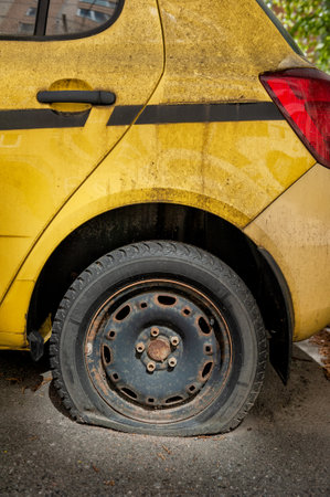 Flat tire on an old abandoned yellow car with a rusted steel wheelの写真素材