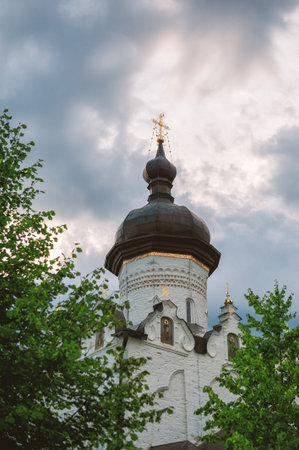 Orthodox church tower with golden dome surrounded by lush green trees under dramatic skyの写真素材