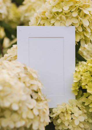 Empty white paper lies on green leaves of a plant with flowers. The blend sheets with botanical...
