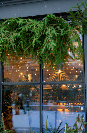 Warm glowing lights reflect through festive seasonal greenery decorates cozy cafe windowの写真素材