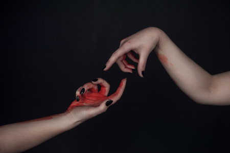 Surreal gesture of hands with black nails and red paint forms mysterious connection in dark minimal sceneの写真素材