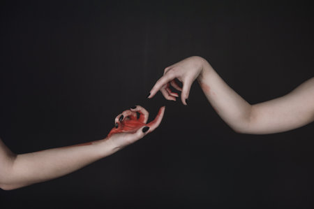 Surreal gesture of hands with black nails and red paint forms mysterious connection in dark minimal sceneの写真素材