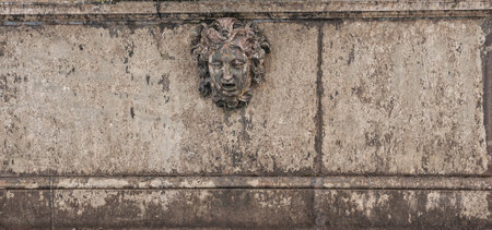 Ancient Medusa sculpture decorates a weathered stone wall with serpentine detailの写真素材