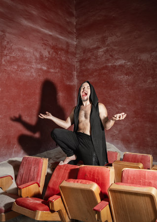 Modern handsome man vampire with drops of blood on his lips screaming in old movie theaterの写真素材