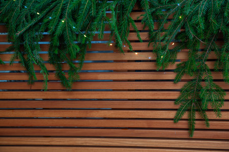 Fresh pine branches hang above wooden wall creating Christmas natural festive textureの写真素材