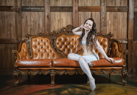 Young beautiful sensual woman wears vintage underwear sitting on the brown leather sofaの写真素材