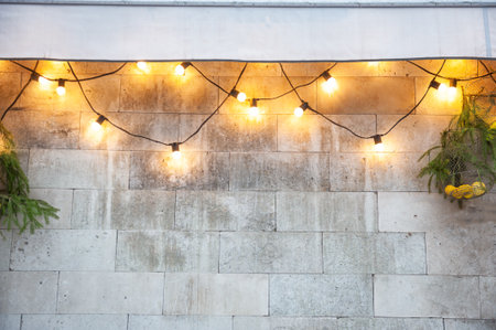 String lights glowing on a stone wall with green pine branches create festive outdoor holiday decor