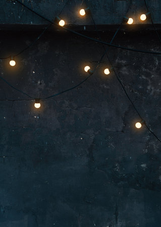 Glowing string lights on a dark concrete wall create a moody and cozy ambiance. Industrial textured...