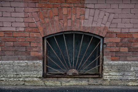Rusty iron bars cover an arched basement window set in aged red brickの写真素材
