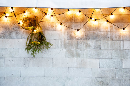 String lights glowing on a stone wall with green pine branches create festive Christmas outdoor holiday decorの写真素材
