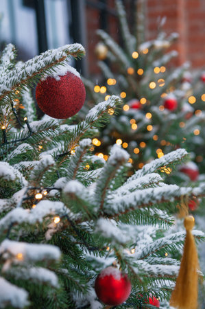 Snow covered Christmas trees with red and gold baubles glow against brick wallsの写真素材