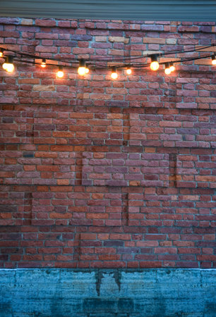 Cozy glowing string lights on a textured red-brick wall backdrop. Warm illumination creates a trendy urban ambiance on rustic bricksの写真素材