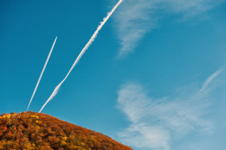 Airplane contrails cut blue sky creating airy dynamic geometryの写真素材