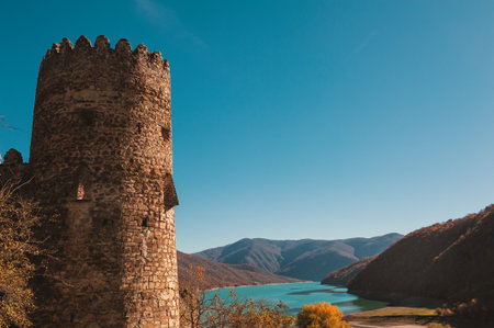 Ancient medieval castle tower overlooks turquoise lake and valleyの写真素材