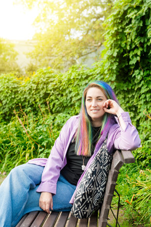 Relaxed woman with colorful hair portrait sitting on park bench outdoorsの写真素材