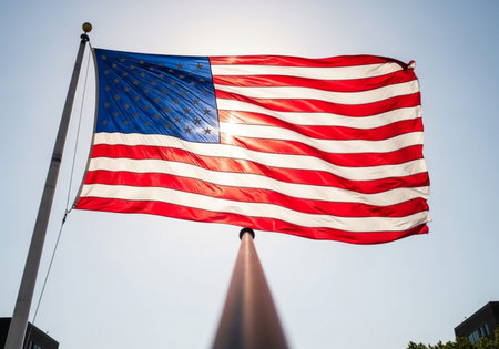 American Flag waving in the wind on a pole with blue sky backgroundの写真素材