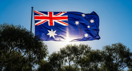 Australia flag waving in the wind with trees in the background on a sunny dayの写真素材