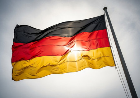 Germany flag waving in the wind against blue sky with sunbeamsの写真素材